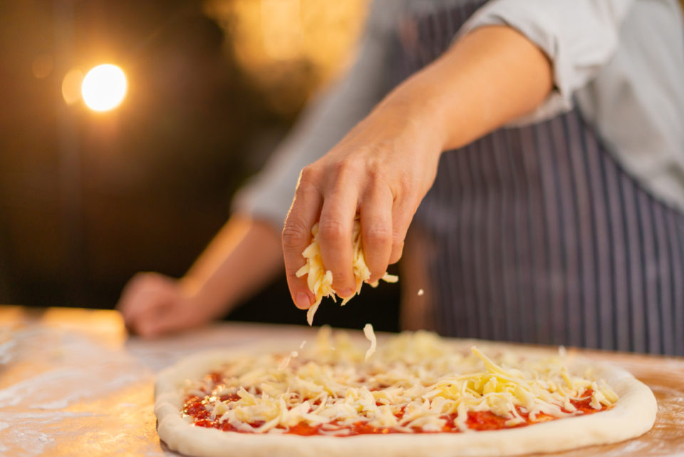 Chef applying cheese to pizza