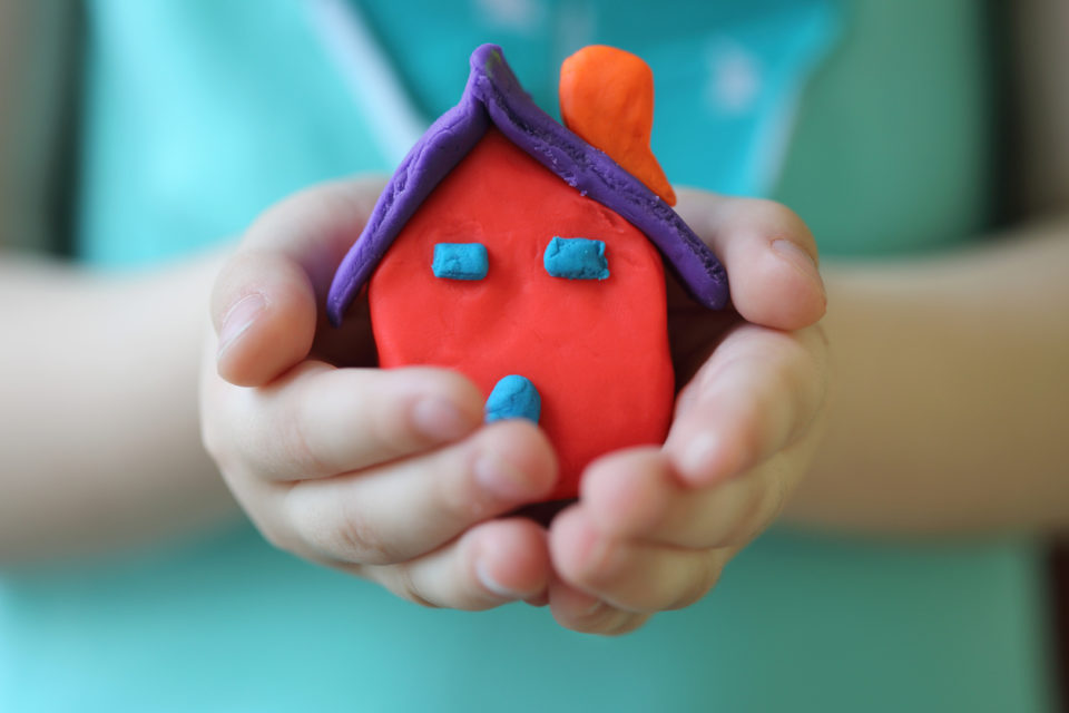 Little kid holding a playdough house with their hands.